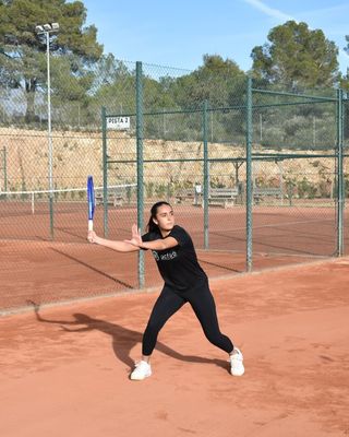 Marta Lopez stretching into a backhand during training on an outdoor clay court